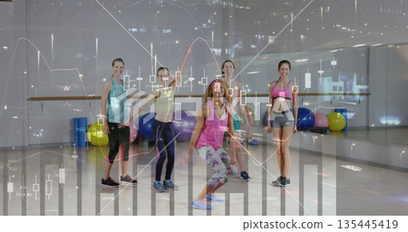 Squatting instructor leading participants in workout studio, with stability balls and ballet bar Squatting instructor leading participants in workout studio, with stability balls and ballet bar 135445419