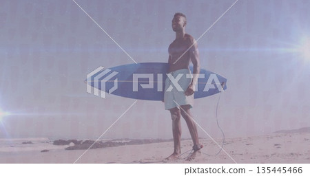 Standing shirtless man in swim trunks holding blue surfboard by waves on sandy beach, lens flares Standing shirtless man in swim trunks holding blue surfboard by waves on sandy beach, lens flares 135445466