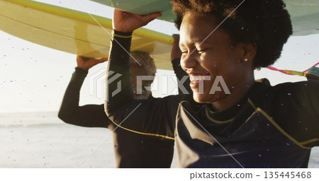 Walking African American woman and man carrying surfboards overhead at shore, with black wetsuits Walking African American woman and man carrying surfboards overhead at shore, with black wetsuits 135445468