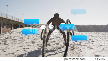 Swinging shirtless man using battle ropes on beach near pier lampposts, with blue chat bubbles Swinging shirtless man using battle ropes on beach near pier lampposts, with blue chat bubbles 135445487