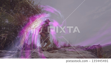 Standing male hiker surveying rocky outcrop on dry grassland hills, with purple light swirl effect Standing male hiker surveying rocky outcrop on dry grassland hills, with purple light swirl effect 135445491