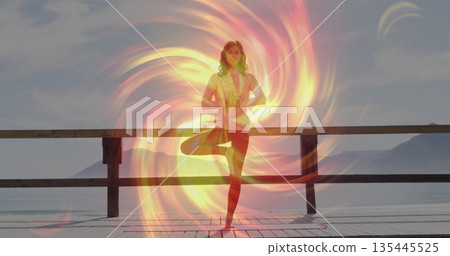 Practicing yoga woman wearing red leggings holding pose on wooden lake pier, with light aura swirl 135445525