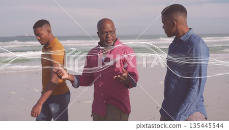 Walking African American trio on wet sand beach, senior man gesturing to men, white wave patterns 135445544