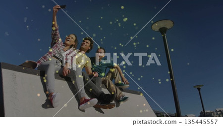 Smiling trio holding smartphone overhead while sitting on concrete ramp under clear blue sky Smiling trio holding smartphone overhead while sitting on concrete ramp under clear blue sky 135445557