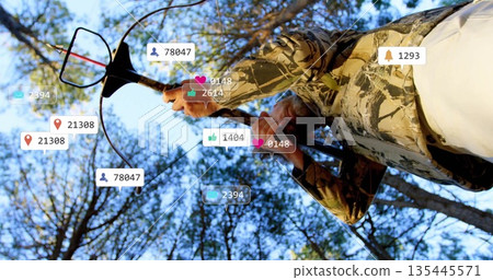 Scanning outdoorsman holding metal detector in pine forest, floating social media icons, copy space Scanning outdoorsman holding metal detector in pine forest, floating social media icons, copy space 135445571