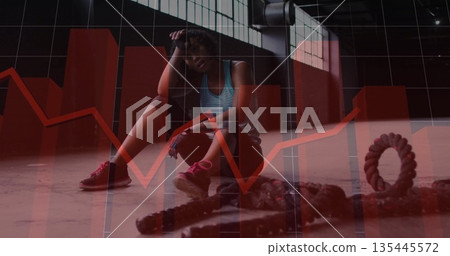 Resting woman in workout clothes lifting hand to forehead on warehouse gym floor, with battle ropes Resting woman in workout clothes lifting hand to forehead on warehouse gym floor, with battle ropes 135445572
