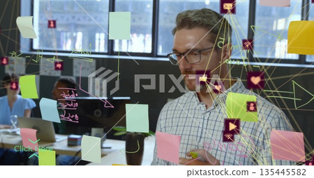Checkered-shirted man writing on glass partition in office, with sticky notes and icons, copy space 135445582