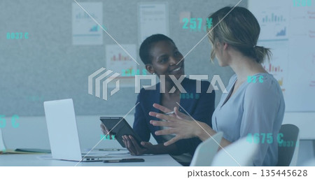 Reviewing two businesswomen analyzing financial charts in conference room, with tablet and laptop Reviewing two businesswomen analyzing financial charts in conference room, with tablet and laptop 135445628