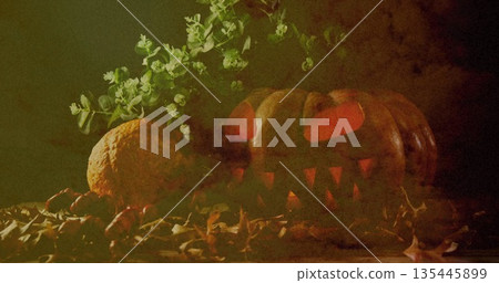 Spooky carved pumpkin glowing among autumn leaves and greenery at night 135445899