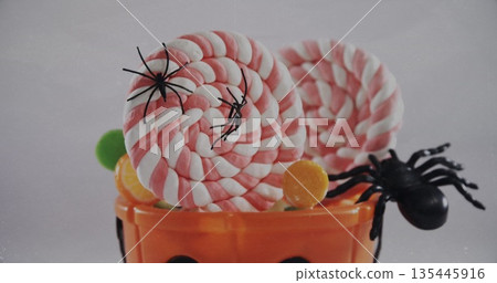 Spiders falling over in halloween pumpkin bucket filled with candies against white background Spiders falling over in halloween pumpkin bucket filled with candies against white background 135445916