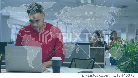 Typing man in red sweater using laptop in open office, with coffee and world map overlay 135446075