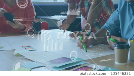 Collaborating professionals reviewing charts at meeting table in modern office, with data overlays 135446221