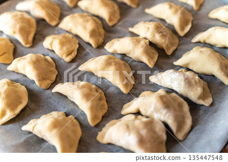 Dumplings are arranged on a baking tray ready for cooking in a kitchen Dumplings are arranged on a baking tray ready for cooking in a kitchen 135447548