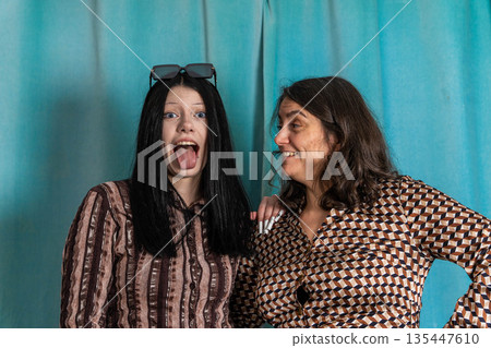 Women share a fun moment with playful expressions in a photo booth setting Women share a fun moment with playful expressions in a photo booth setting 135447610