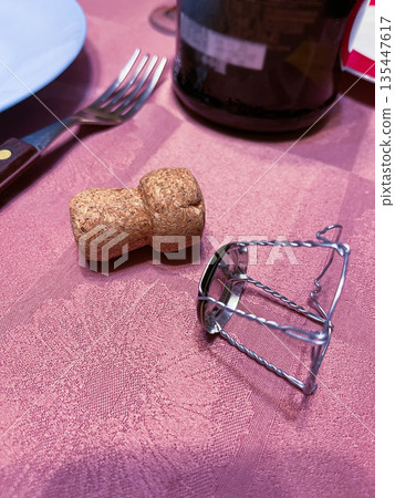 Cork and cage placed on a table with a fork and wine bottle in the background 135447617