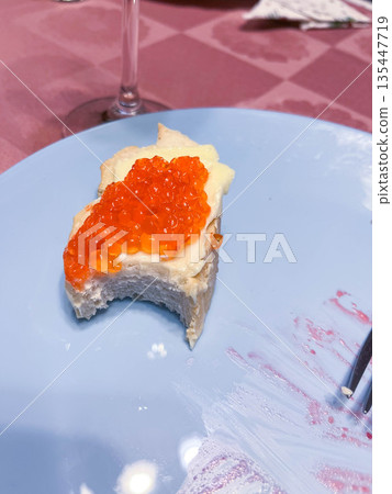 Fresh bread with butter and fish roe on a blue plate at a dinner table 135447719