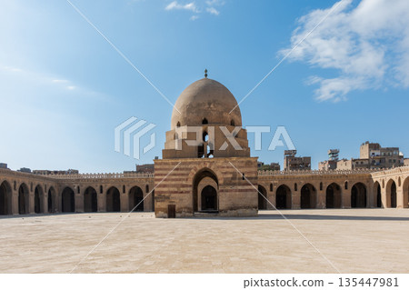Ibn Tulun Mosque in Cairo features a large dome and intricate architectural details. The structure showcases Islamic design elements and historical significance. Ibn Tulun Mosque in Cairo features a large dome and intricate architectural details. The structure showcases Islamic design elements and historical significance. 135447981