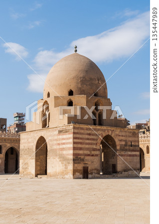 Ibn Tulun Mosque in Cairo features a large dome and intricate architectural details. The structure showcases Islamic design elements and historical significance. Ibn Tulun Mosque in Cairo features a large dome and intricate architectural details. The structure showcases Islamic design elements and historical significance. 135447989