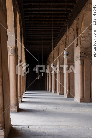 A corridor in the Ibn Tulun mosque with tall columns and intricate patterns. Soft light filters through, creating shadows. A corridor in the Ibn Tulun mosque with tall columns and intricate patterns. Soft light filters through, creating shadows. 135448040