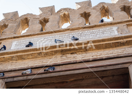 Pigeons perched on the ornate entrance of a mosque. The structure features intricate architectural details and a clear blue sky in the background. Pigeons perched on the ornate entrance of a mosque. The structure features intricate architectural details and a clear blue sky in the background. 135448042