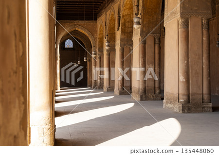 Ibn Tulun Mosque in Cairo features arched corridors with sunlight streaming through. The architecture showcases Islamic design elements and historical significance. Ibn Tulun Mosque in Cairo features arched corridors with sunlight streaming through. The architecture showcases Islamic design elements and historical significance. 135448060