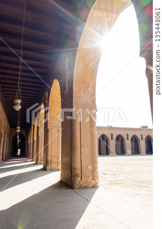Ibn Tulun Mosque in Cairo features arched corridors with sunlight streaming through. The architecture showcases Islamic design elements and historical significance. 135448061