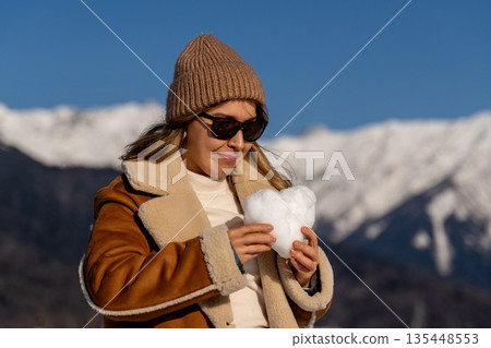 Snow Heart Mountains Woman Winter: Happy woman makes snow heart in snowy mountains during winter. Snow Heart Mountains Woman Winter: Happy woman makes snow heart in snowy mountains during winter. 135448553
