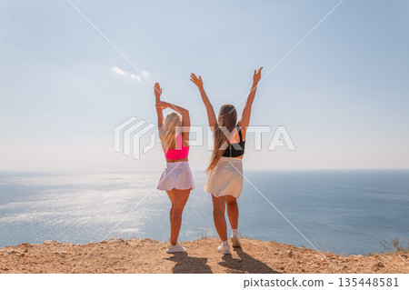 Two women standing on a hill overlooking the ocean, one wearing a pink top Two women standing on a hill overlooking the ocean, one wearing a pink top 135448581