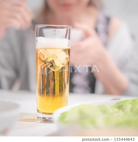 A glass of ice-cold golden beer in close-up, and blurred woman in the background A glass of ice-cold golden beer in close-up, and blurred woman in the background 135449643