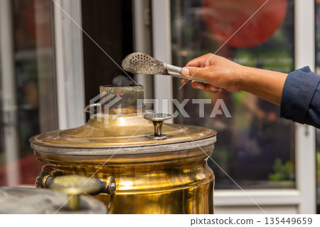 Person using tongs to prepare charcoal samovar outdoors Person using tongs to prepare charcoal samovar outdoors 135449659