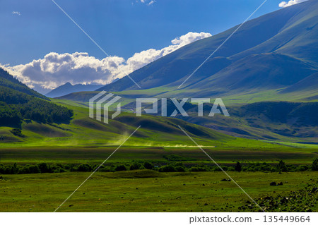 Car with cloud of dust crossing majestic landscape of green hills and mountains under blue sky in Kyrgyzstan Car with cloud of dust crossing majestic landscape of green hills and mountains under blue sky in Kyrgyzstan 135449664