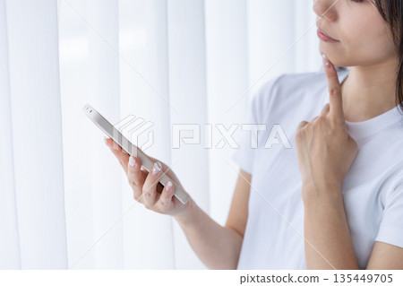 年輕女子拿著智慧型手機思考 年輕女子拿著智慧型手機思考 135449705