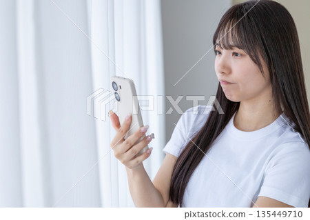 年輕女子拿著智慧型手機思考 年輕女子拿著智慧型手機思考 135449710