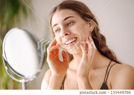 Young woman with problem skin looking into mirror. Concept of acne therapy, scars 135449766