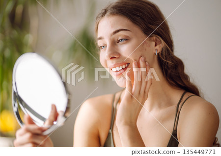 Young woman with problem skin looking into mirror. Concept of acne therapy, scars 135449771