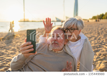 Video call. Senior couple making selfie having video call on beach outdoor. Mature old grandmother grandfather talking speaking online. Older generation modern tech usage. Virtual meeting online chat Video call. Senior couple making selfie having video call on beach outdoor. Mature old grandmother grandfather talking speaking online. Older generation modern tech usage. Virtual meeting online chat 135449980