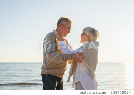 Senior mature couple hugging enjoying outdoor recreation walking on beach. Old husband wife embracing with tenderness love enjoying sweet bonding. Grandmother grandfather together. Family moment love Senior mature couple hugging enjoying outdoor recreation walking on beach. Old husband wife embracing with tenderness love enjoying sweet bonding. Grandmother grandfather together. Family moment love 135450024