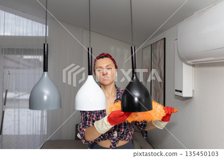 Woman Dusts Pendant Lights in Apartment During Daytime Cleaning Woman Dusts Pendant Lights in Apartment During Daytime Cleaning 135450103