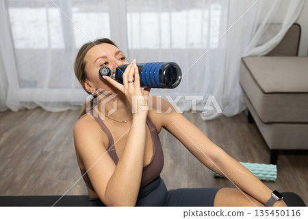Woman Drinking Water From a Blue Bottle After Exercising at Home Woman Drinking Water From a Blue Bottle After Exercising at Home 135450116