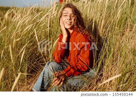 Happy woman enjoying nature outdoors in tall grass. Flying hairs. Outdoor. Fashion style. 135450144