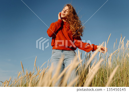 Happy woman enjoying nature outdoors in tall grass. Flying hairs. Outdoor. Fashion style. 135450145