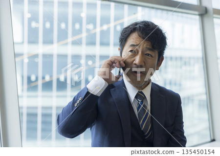 A middle-aged businessman who makes a phone call with a smartphone A middle-aged businessman who makes a phone call with a smartphone 135450154