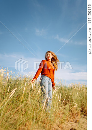 Happy woman enjoying nature outdoors in tall grass. Flying hairs. Outdoor. Fashion style. 135450156