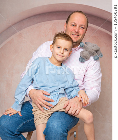 Studio portrait of a father holding his young son. Warm tones, soft light and relaxed poses. Concept of family, fatherhood, parenting and happy childhood 135450291