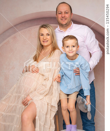 Studio portrait of parents with their child, highlighting pregnancy and family connection. Soft light and neutral background. Concept of love, care and expecting a baby Studio portrait of parents with their child, highlighting pregnancy and family connection. Soft light and neutral background. Concept of love, care and expecting a baby 135450294