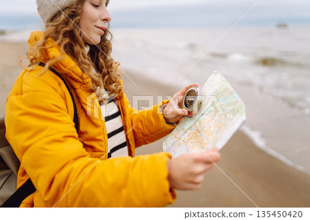 Traveler explorer young woman holding compass, map in hands on beach near the sea. Active lifestyle. Traveler explorer young woman holding compass, map in hands on beach near the sea. Active lifestyle. 135450420