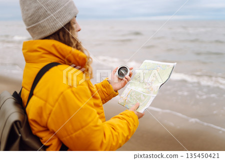 Traveler explorer young woman holding compass, map in hands on beach near the sea. Active lifestyle. Traveler explorer young woman holding compass, map in hands on beach near the sea. Active lifestyle. 135450421