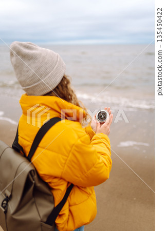 Woman traveler looking for directions with a compass on beach. Active lifestyle. Adventure concept. Woman traveler looking for directions with a compass on beach. Active lifestyle. Adventure concept. 135450422