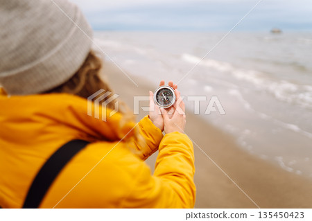 Woman traveler looking for directions with a compass on beach. Active lifestyle. Adventure concept. Woman traveler looking for directions with a compass on beach. Active lifestyle. Adventure concept. 135450423