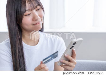 年輕女子手持智慧型手機和信用卡 年輕女子手持智慧型手機和信用卡 135450535